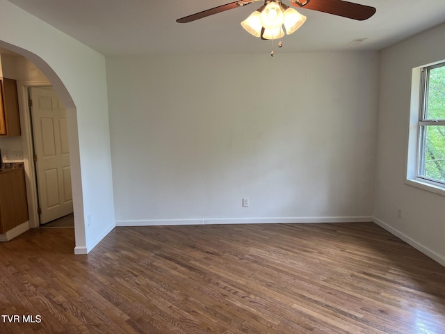 unfurnished room with wood finished floors, a ceiling fan, baseboards, and arched walkways