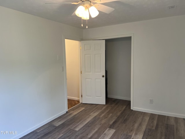 unfurnished bedroom with a closet, dark wood-style flooring, a ceiling fan, and baseboards