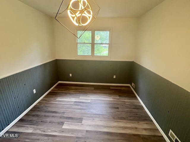 unfurnished dining area featuring wood finished floors, an inviting chandelier, wainscoting, visible vents, and wooden walls