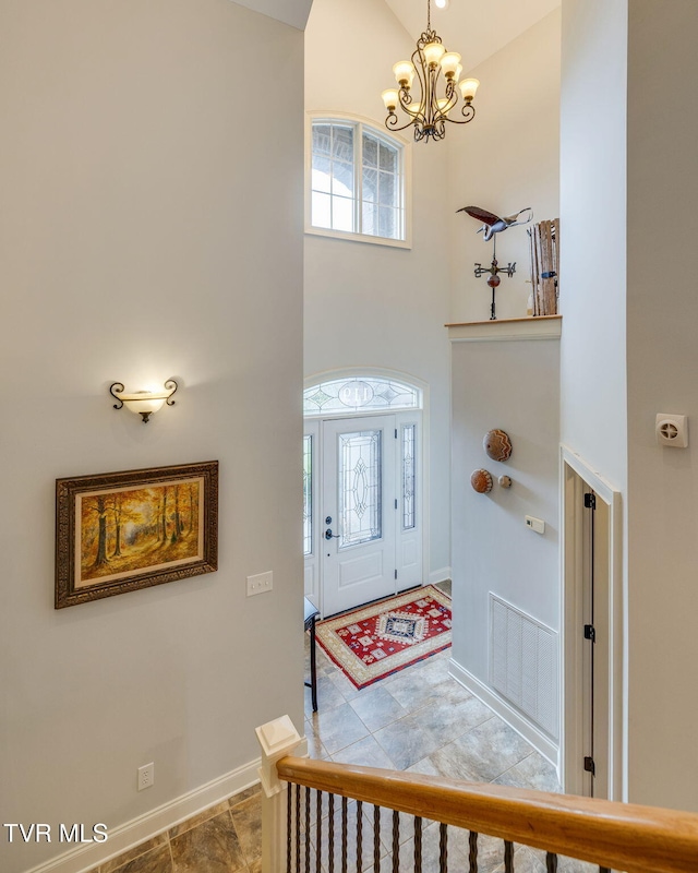 foyer entrance with visible vents, baseboards, a chandelier, a high ceiling, and a wealth of natural light