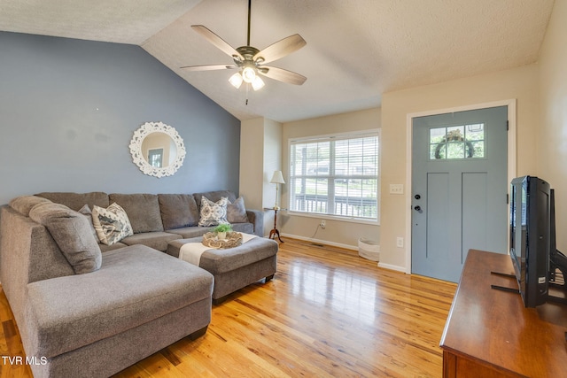living area with a textured ceiling, ceiling fan, baseboards, light wood-type flooring, and vaulted ceiling