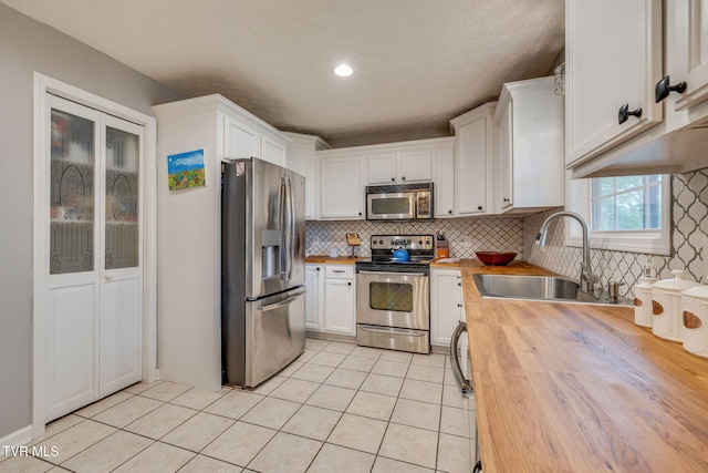 kitchen featuring light tile patterned floors, wood counters, stainless steel appliances, white cabinets, and a sink