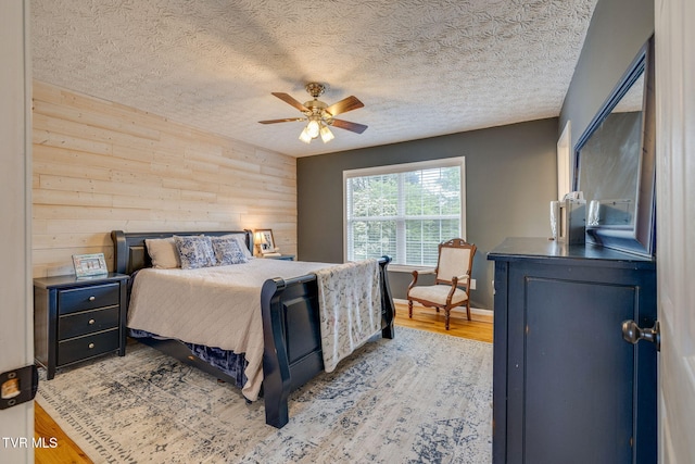 bedroom featuring a textured ceiling, a ceiling fan, wood walls, and wood finished floors