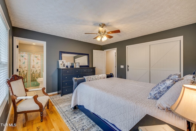 bedroom with ensuite bath, a closet, baseboards, light wood-type flooring, and a textured ceiling