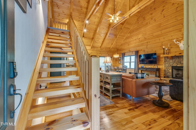 stairs with wood-type flooring, a fireplace, wooden walls, high vaulted ceiling, and wooden ceiling