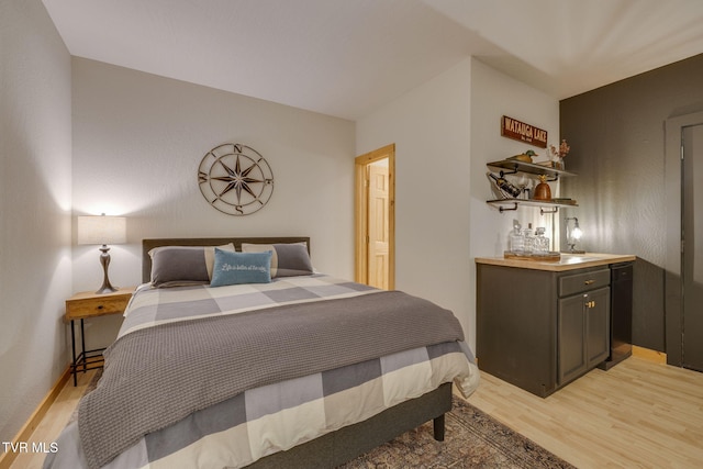 bedroom with baseboards, light wood finished floors, and bar