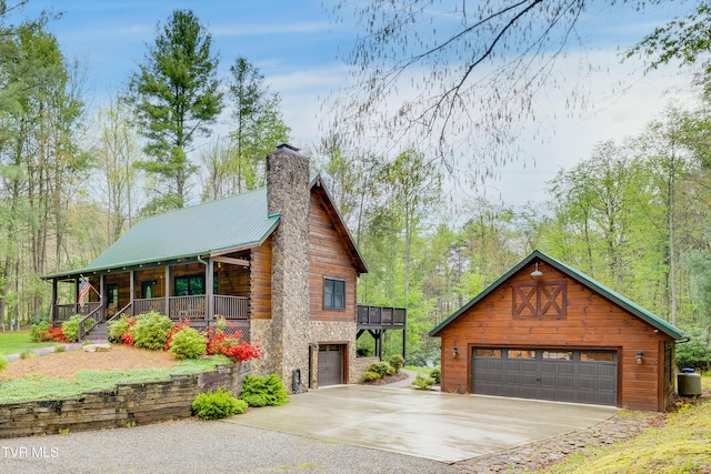 exterior space with stone siding, a garage, a chimney, covered porch, and metal roof