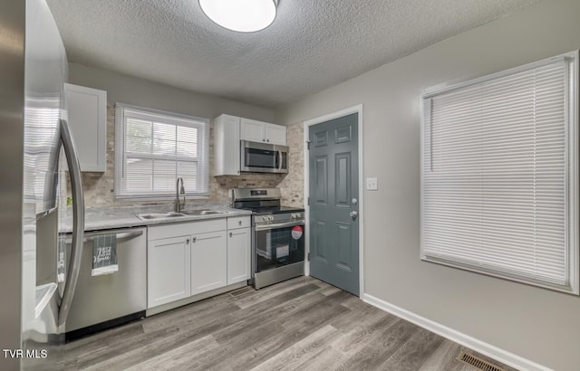kitchen with appliances with stainless steel finishes, backsplash, a sink, white cabinetry, and a textured ceiling