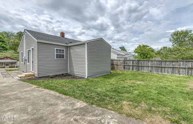 exterior space featuring fence, a chimney, a lawn, and a shingled roof
