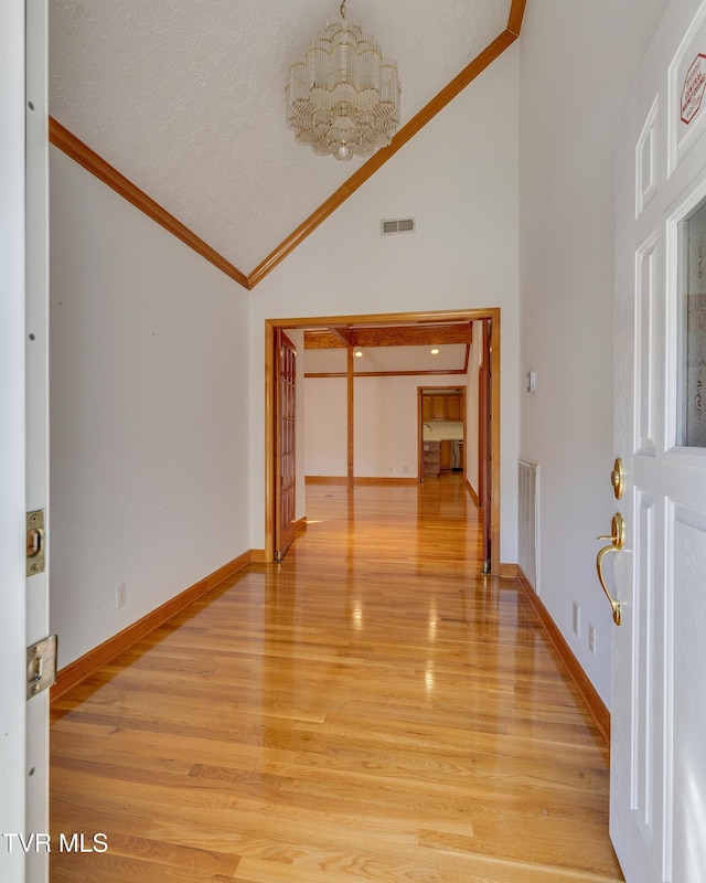 interior space with light wood-style flooring, a chandelier, visible vents, crown molding, and high vaulted ceiling