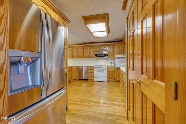kitchen featuring a textured ceiling, light wood-style flooring, stainless steel appliances, light countertops, and brown cabinetry