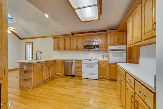 kitchen with lofted ceiling, a sink, appliances with stainless steel finishes, light wood-style floors, and a peninsula