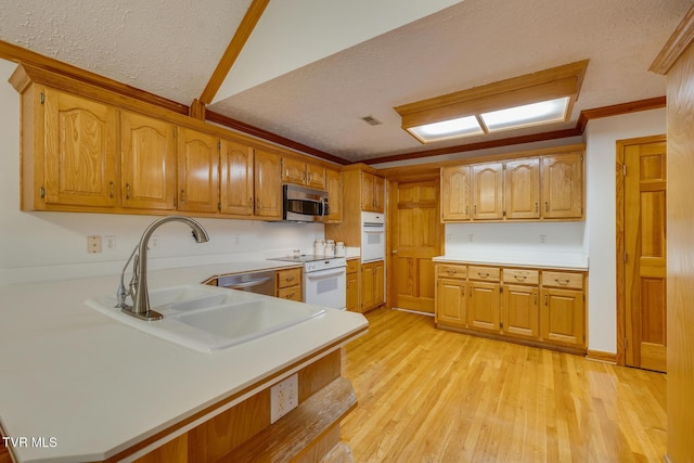 kitchen featuring light wood finished floors, a sink, light countertops, a textured ceiling, and appliances with stainless steel finishes