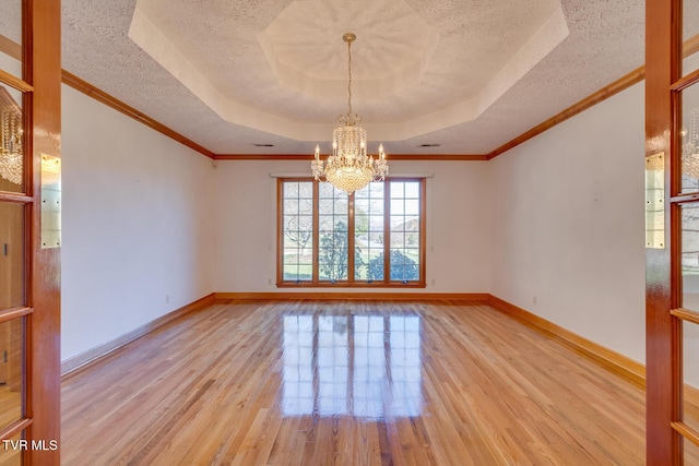 spare room with a textured ceiling, wood finished floors, a tray ceiling, and a chandelier
