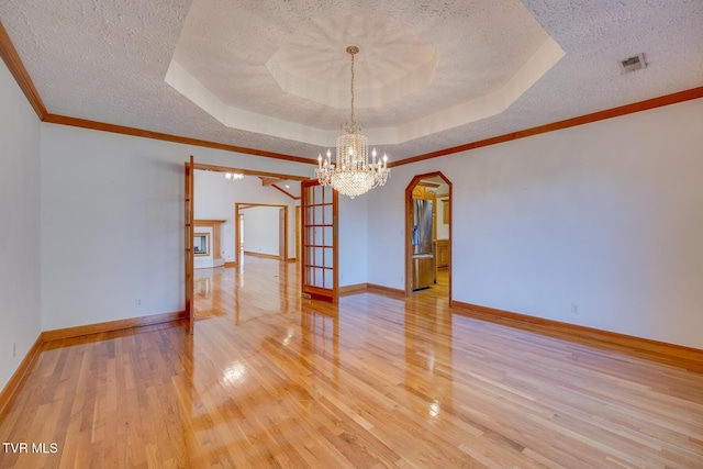 empty room featuring light wood-style floors, a notable chandelier, a tray ceiling, visible vents, and a textured ceiling