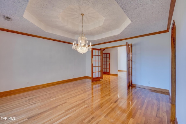 empty room featuring a textured ceiling, visible vents, a raised ceiling, and light wood-style floors