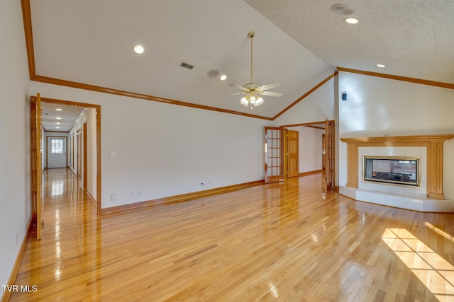 unfurnished living room featuring a tile fireplace, light wood-style floors, crown molding, visible vents, and baseboards
