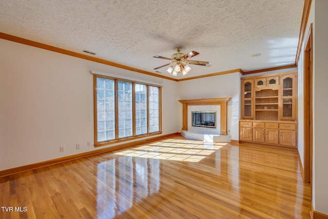 unfurnished living room featuring light wood finished floors, a tile fireplace, ceiling fan, crown molding, and a textured ceiling