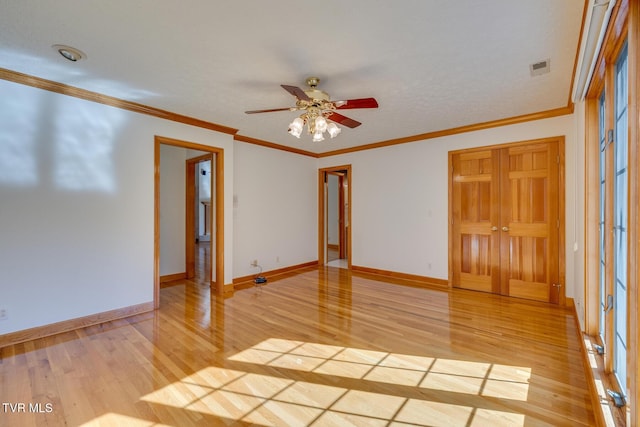 spare room with light wood finished floors, crown molding, a ceiling fan, visible vents, and baseboards