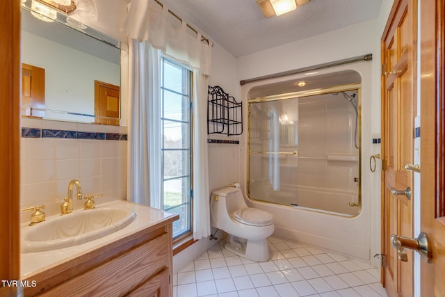 bathroom with tile patterned flooring, combined bath / shower with glass door, tile walls, toilet, and vanity