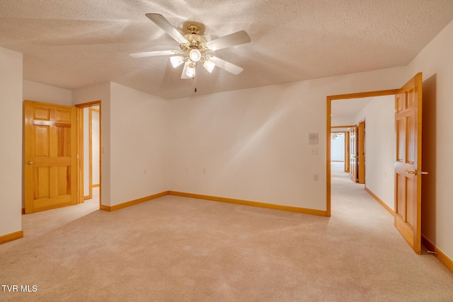 spare room featuring a textured ceiling, ceiling fan, baseboards, and light carpet