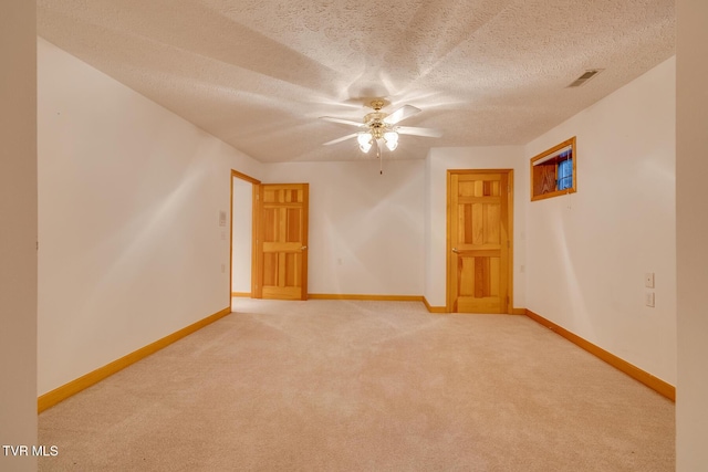 carpeted spare room featuring a textured ceiling, visible vents, a ceiling fan, and baseboards