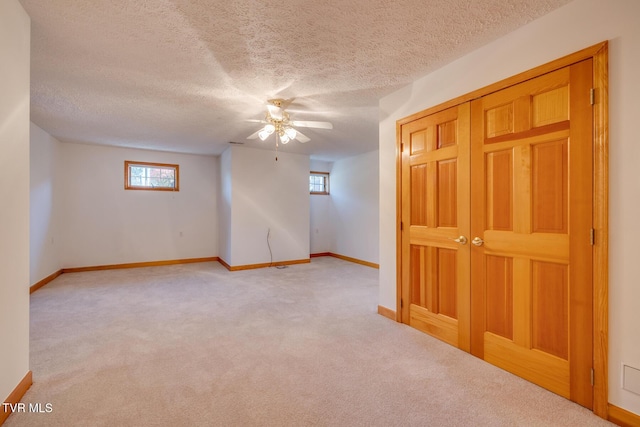 empty room featuring a textured ceiling, ceiling fan, light colored carpet, and baseboards
