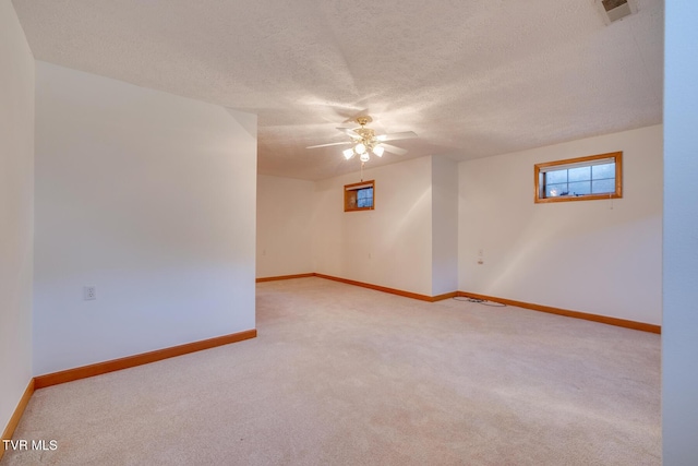 carpeted empty room with a textured ceiling, visible vents, ceiling fan, and baseboards