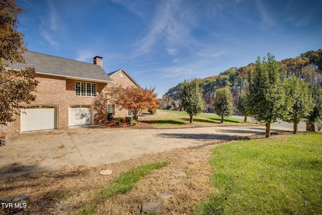 view of side of property featuring a chimney, a yard, brick siding, a garage, and driveway