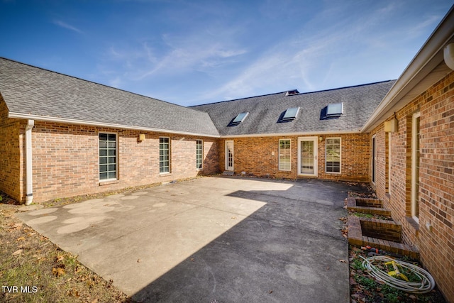 rear view of property with a patio area, a shingled roof, and brick siding