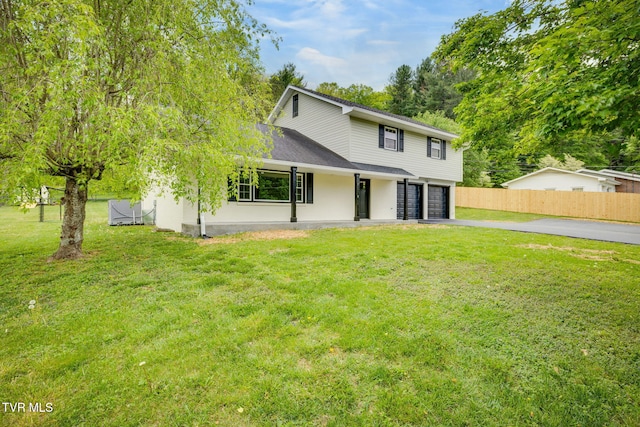 traditional home featuring fence, aphalt driveway, a shingled roof, a garage, and a front yard