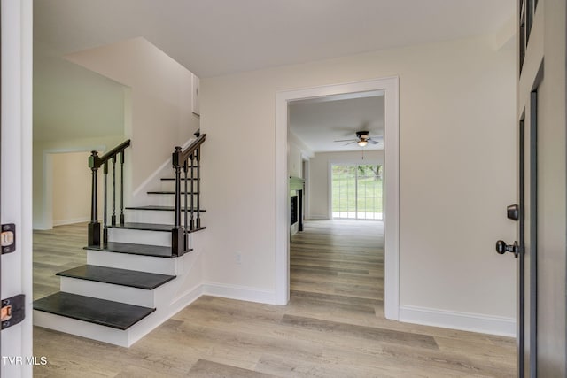 foyer entrance with wood finished floors, stairs, ceiling fan, a fireplace, and baseboards