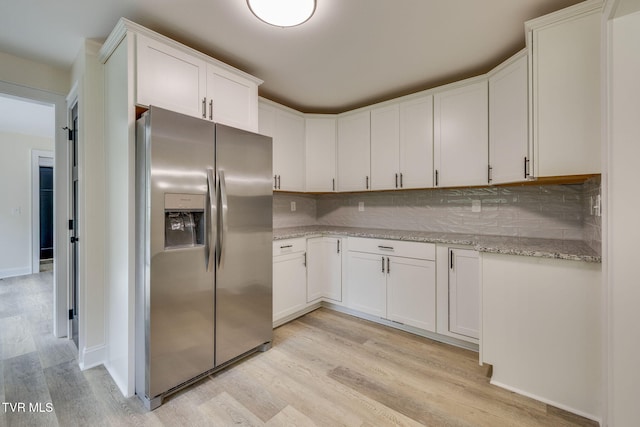 kitchen with light stone countertops, light wood-style floors, stainless steel fridge with ice dispenser, white cabinets, and backsplash
