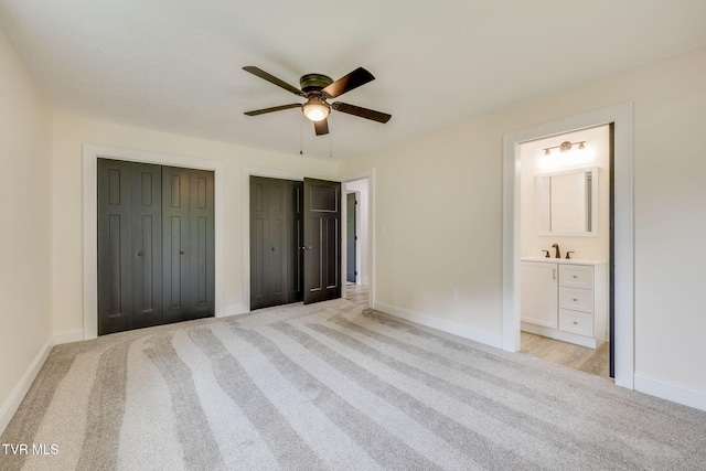 unfurnished bedroom featuring baseboards, light carpet, connected bathroom, and two closets