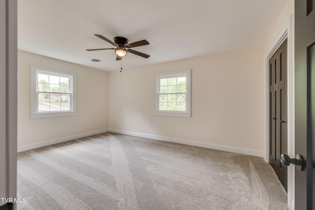 carpeted spare room with baseboards, visible vents, ceiling fan, and plenty of natural light