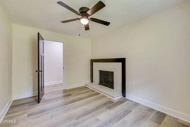 unfurnished living room featuring baseboards, light wood-type flooring, a ceiling fan, and a brick fireplace