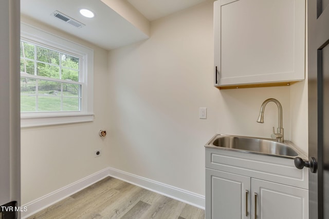 clothes washing area featuring light wood-style flooring, electric dryer hookup, cabinet space, a sink, and visible vents
