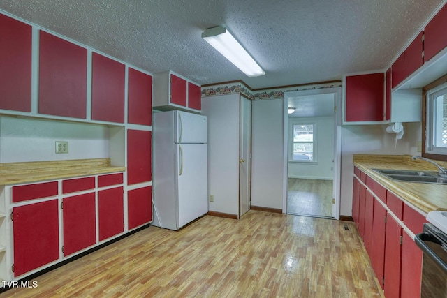 kitchen with red cabinetry, a sink, freestanding refrigerator, and light wood-style floors