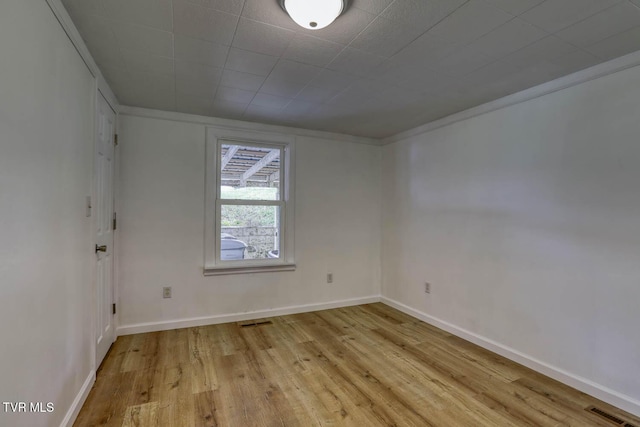 empty room with light wood-style floors, ornamental molding, and visible vents