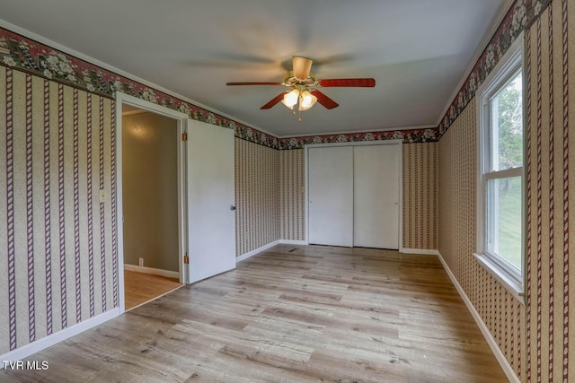 unfurnished bedroom featuring multiple windows, wallpapered walls, and wood finished floors