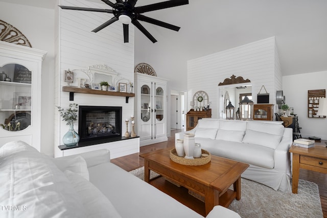 living area featuring wood finished floors, high vaulted ceiling, ceiling fan, and a fireplace