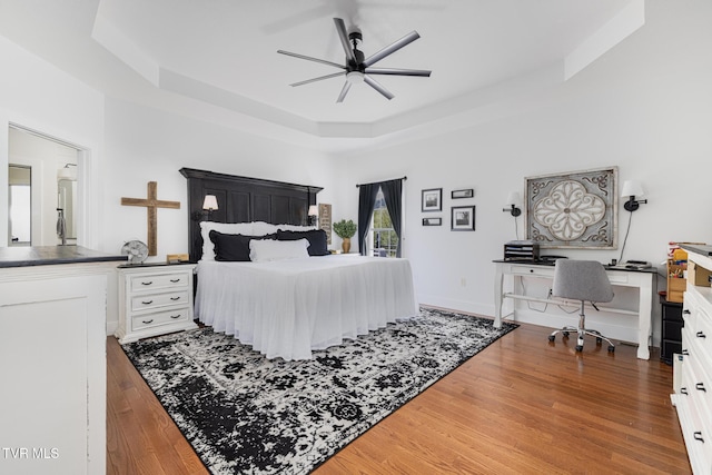 bedroom featuring ceiling fan, wood finished floors, and a raised ceiling