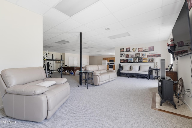 living area featuring carpet, a wood stove, and a paneled ceiling