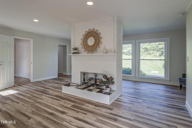 unfurnished living room with baseboards, a brick fireplace, recessed lighting, and wood finished floors