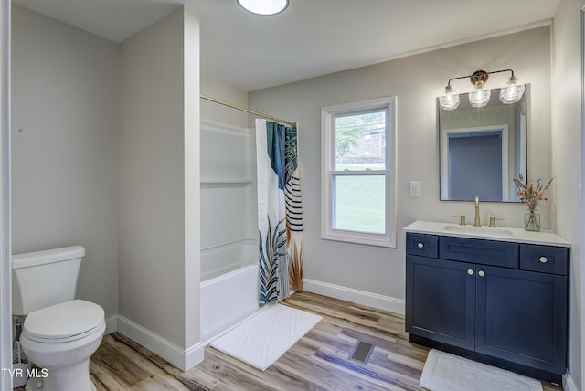 bathroom with vanity, toilet, baseboards, wood finished floors, and shower / tub combo