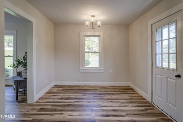 unfurnished dining area featuring baseboards, wood finished floors, and a notable chandelier