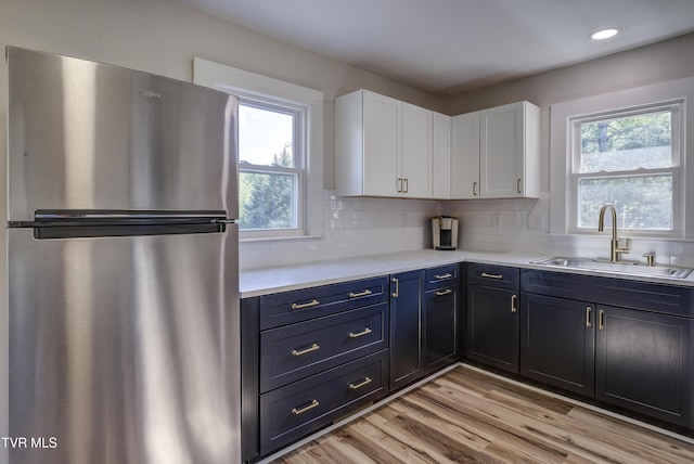 kitchen featuring a sink, freestanding refrigerator, white cabinetry, and a wealth of natural light