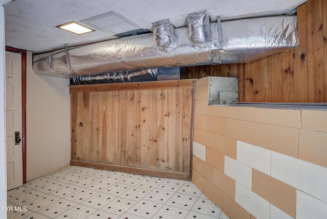 basement featuring light floors and wooden walls