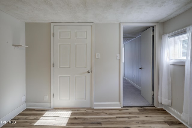 unfurnished bedroom with a closet, a textured ceiling, baseboards, and light wood-style floors