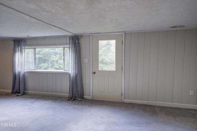 interior space with visible vents, a textured ceiling, baseboards, and wooden walls